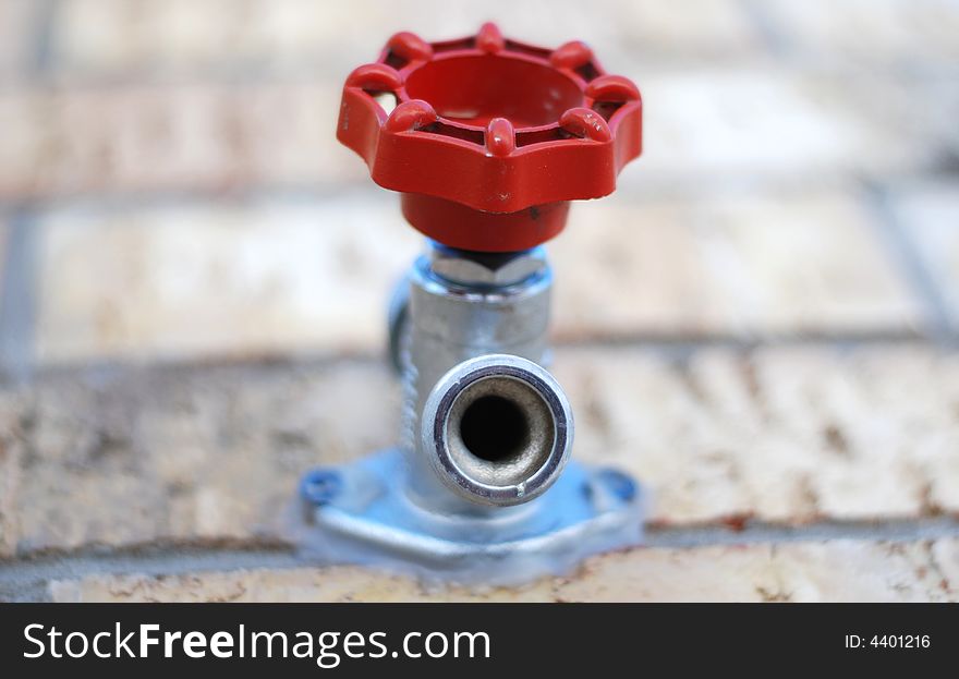 Outdoor water spigot with a red handle attached to a brick wall. Shallow DOF