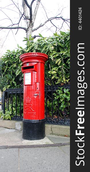 Bright red British pillar box against background of evergreen leaves . Bright red British pillar box against background of evergreen leaves
