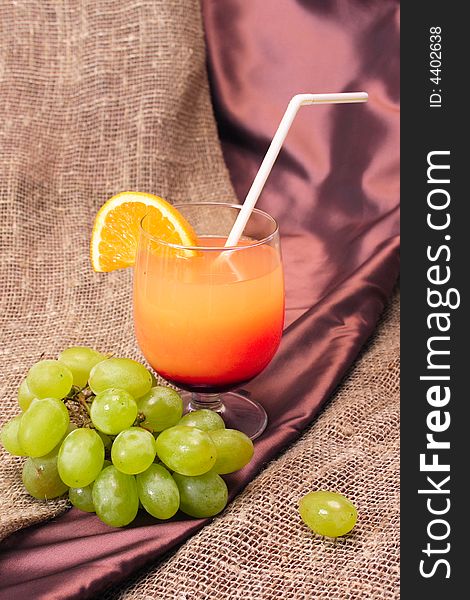 A picture of an orange cocktail with a branch of grape. A picture of an orange cocktail with a branch of grape