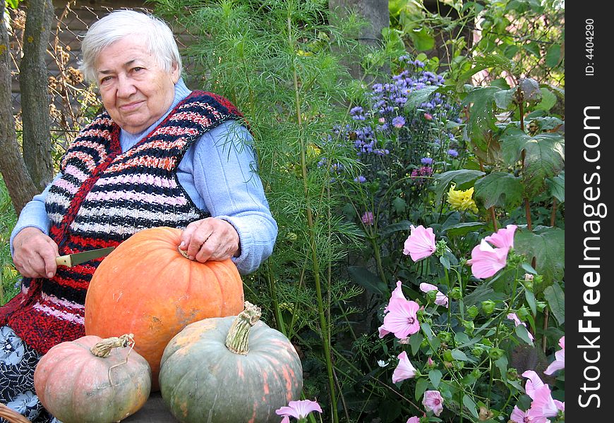 The old woman is sitting on the bench and cutting the pumpkins. The old woman is sitting on the bench and cutting the pumpkins