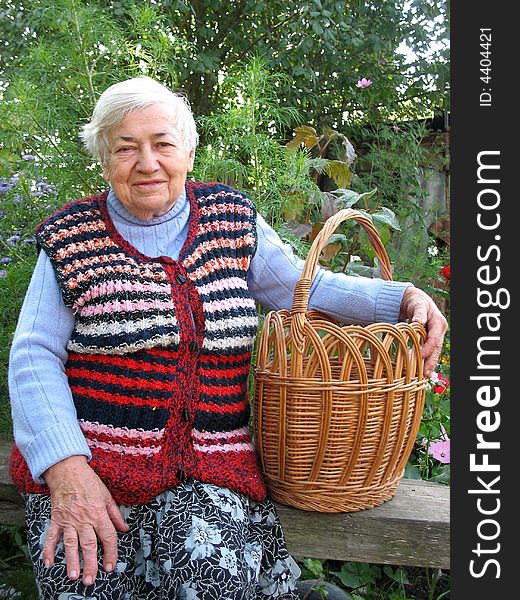 The old woman is sitting on the bench and holding the basket. The old woman is sitting on the bench and holding the basket