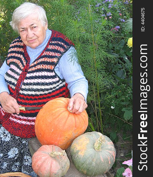 The old woman is sitting on the bench and cutting the pumpkins. The old woman is sitting on the bench and cutting the pumpkins