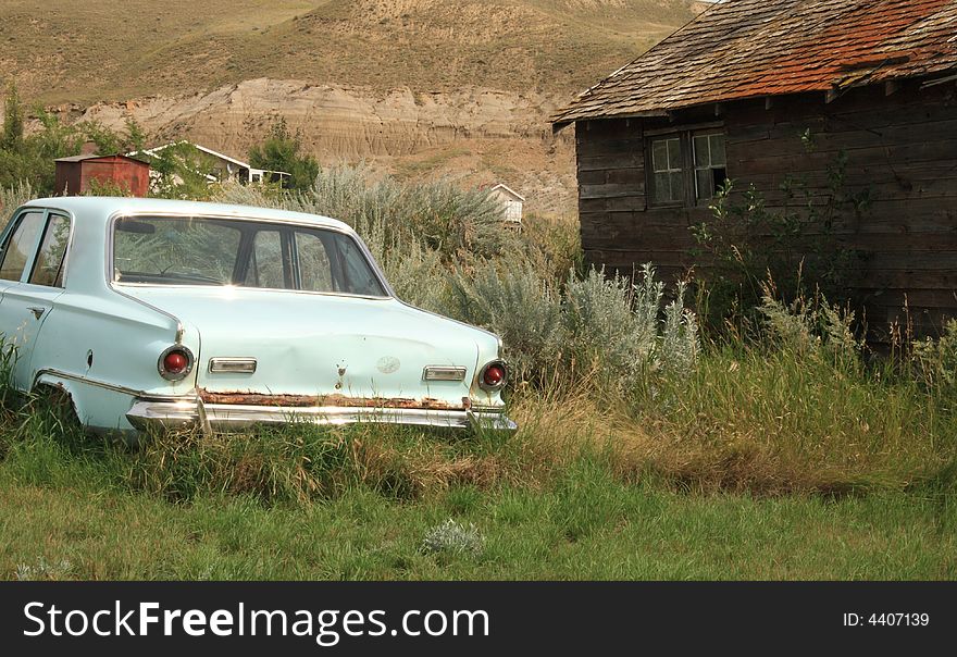 An old abandoned car sitting in the weeds in a ghost town. An old abandoned car sitting in the weeds in a ghost town