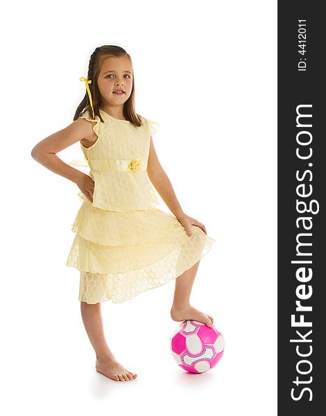 Little girl in a pretty yellow dress with her bare foot on a pink soccer ball. One of series. Studio shot isolated on a white background. Little girl in a pretty yellow dress with her bare foot on a pink soccer ball. One of series. Studio shot isolated on a white background.