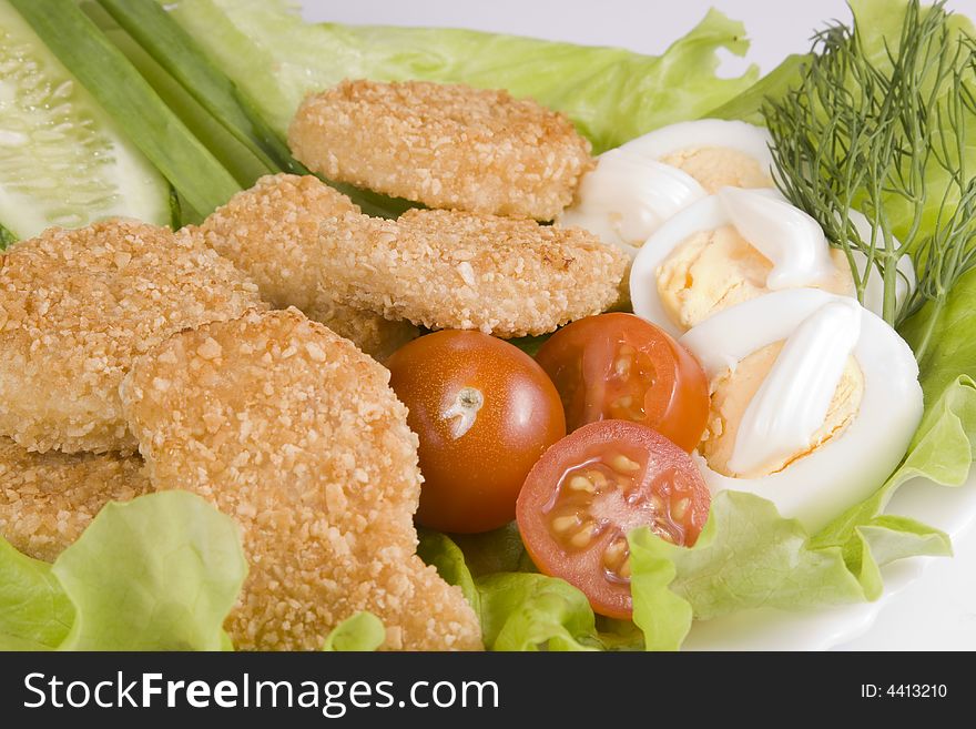 Appetizing fried chicken nuggets, egg with mayonnaise, tomatoes, cucumbers and onions on salad leaves. Close-up. Selective focus. Appetizing fried chicken nuggets, egg with mayonnaise, tomatoes, cucumbers and onions on salad leaves. Close-up. Selective focus.