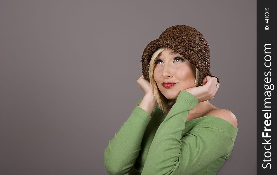 A blonde model in brown hat and green blouse looking up against grey background. A blonde model in brown hat and green blouse looking up against grey background