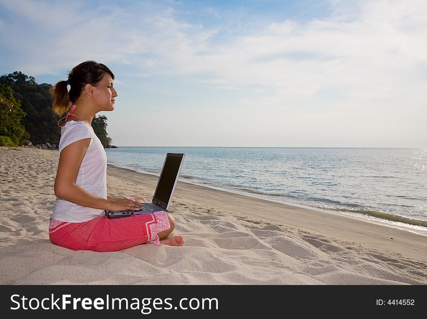 Young woman working on her laptop facing a beautiful beach. Young woman working on her laptop facing a beautiful beach