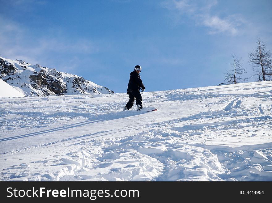 The snowboarder goes for a drive in mountains on a background of the blue sky