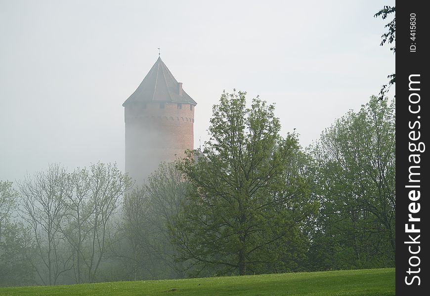 Tower of castle in evening haze behind trees