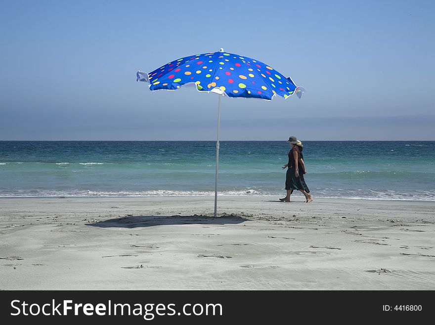 Two women walking by the seashore and a beach umbrella. Two women walking by the seashore and a beach umbrella