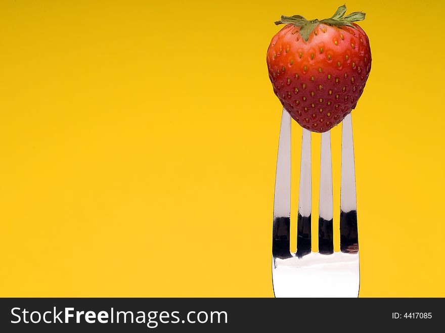 A fresh red strawberry on a fork against a graphic yellow background. A fresh red strawberry on a fork against a graphic yellow background