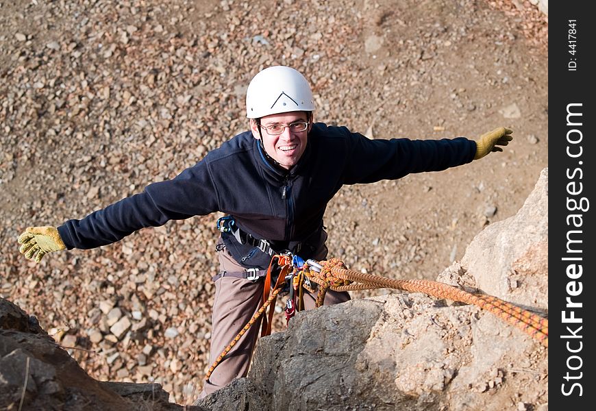 Climber hanging on the rock with arms wide open with happy face