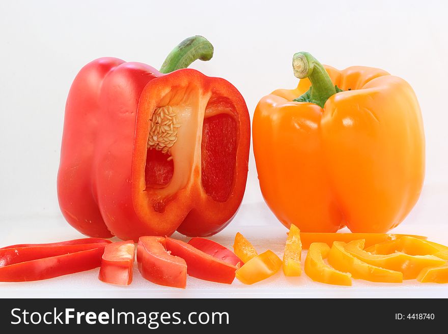 A red and a yellow bell pepper on a white cutting board with fresh cut slices in front. Isolated on a white background. A red and a yellow bell pepper on a white cutting board with fresh cut slices in front. Isolated on a white background.