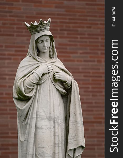 Angel statue with crown in front of red brick wall.