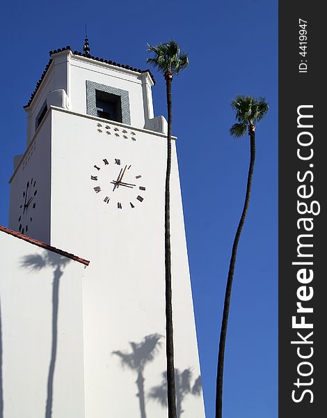 Architectural detail of Union Station's Spanish style clock tower with two palm trees against blue sky. Architectural detail of Union Station's Spanish style clock tower with two palm trees against blue sky