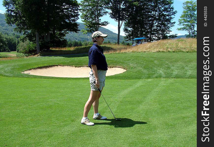 A lady golfer looks on as her golf ball approaches the hole. A lady golfer looks on as her golf ball approaches the hole.