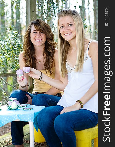 Beautiful teen sisters remembering childhood with their old tea set. Focus on dark haired sister. Beautiful teen sisters remembering childhood with their old tea set. Focus on dark haired sister.