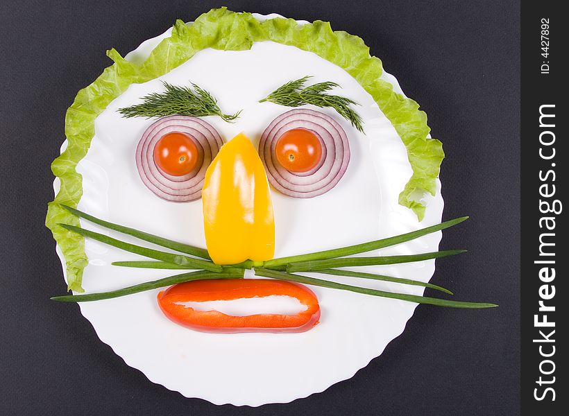 Smiling face from fresh appetizing vegetables on a white plate. On a black background. Smiling face from fresh appetizing vegetables on a white plate. On a black background.