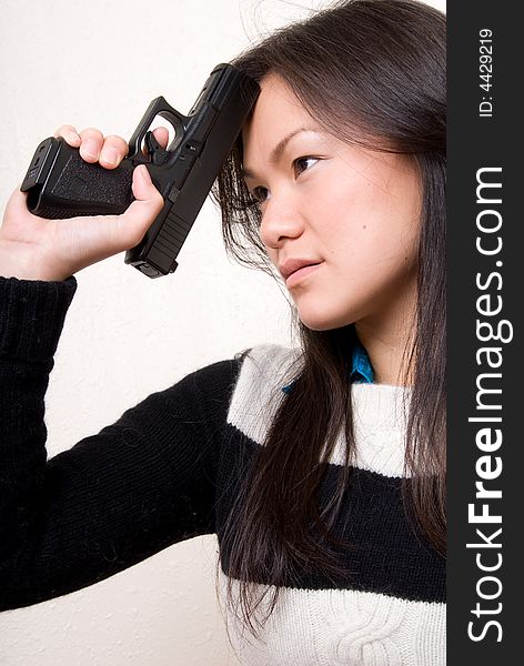 An Asian female resting a tip of a gun on her head as if she is thinking about something bad. An Asian female resting a tip of a gun on her head as if she is thinking about something bad.