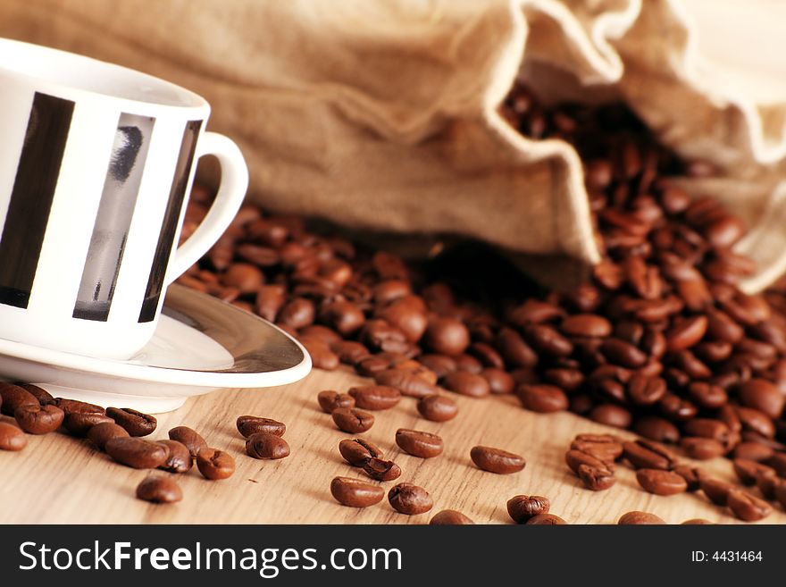Some coffee beans and a jute sack behind a cup of black coffee. Some coffee beans and a jute sack behind a cup of black coffee