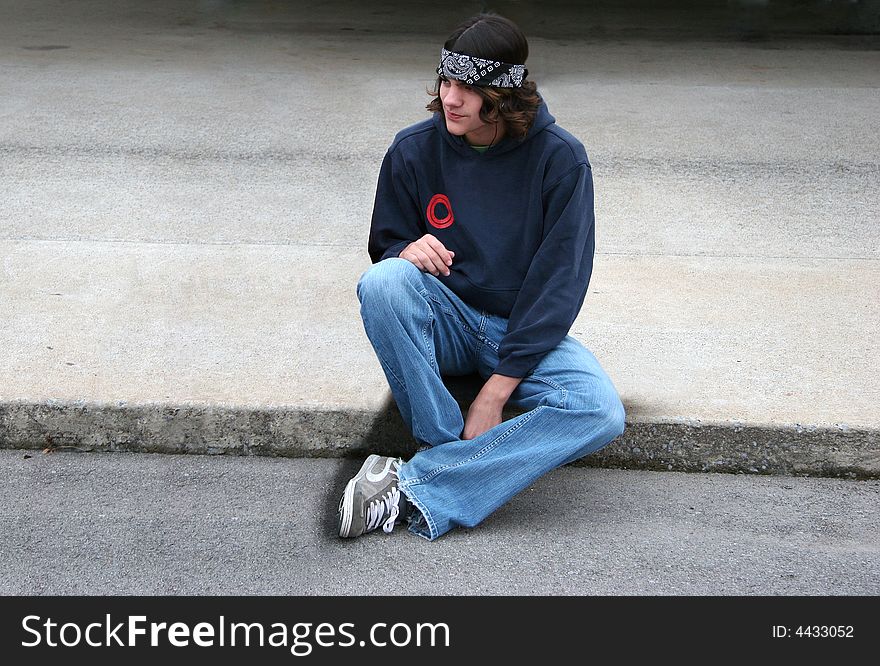 Handsome male teenager sitting on concrete listening to music. Handsome male teenager sitting on concrete listening to music.