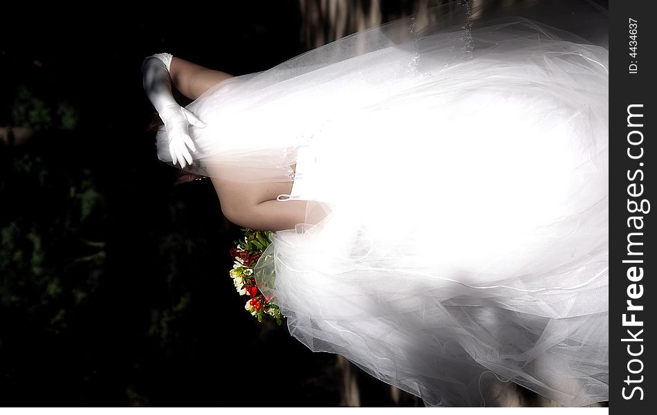 The back of a bride in white holding a bouquet and straightening her veil. The back of a bride in white holding a bouquet and straightening her veil.