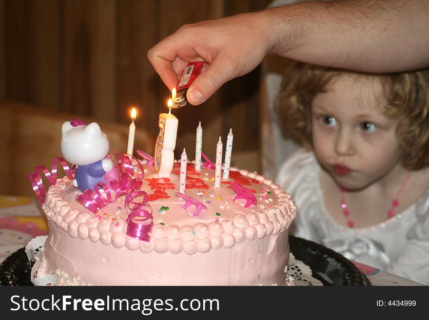 Little red haired girl looks on as candles on her birthday cake are being lit. Little red haired girl looks on as candles on her birthday cake are being lit.