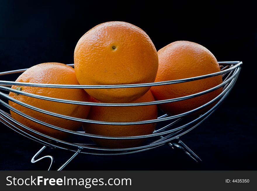 Stainless steel wire basket containing four oranges. Stainless steel wire basket containing four oranges