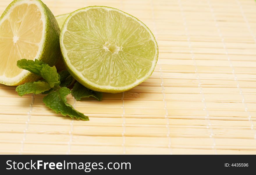 Closeup of three bright yellow lemons and lime on wooden placemat- shallow depth of field. Closeup of three bright yellow lemons and lime on wooden placemat- shallow depth of field