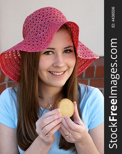 Pretty girl wearing red hat smiling as she holds round cookie at outside cafe. Pretty girl wearing red hat smiling as she holds round cookie at outside cafe