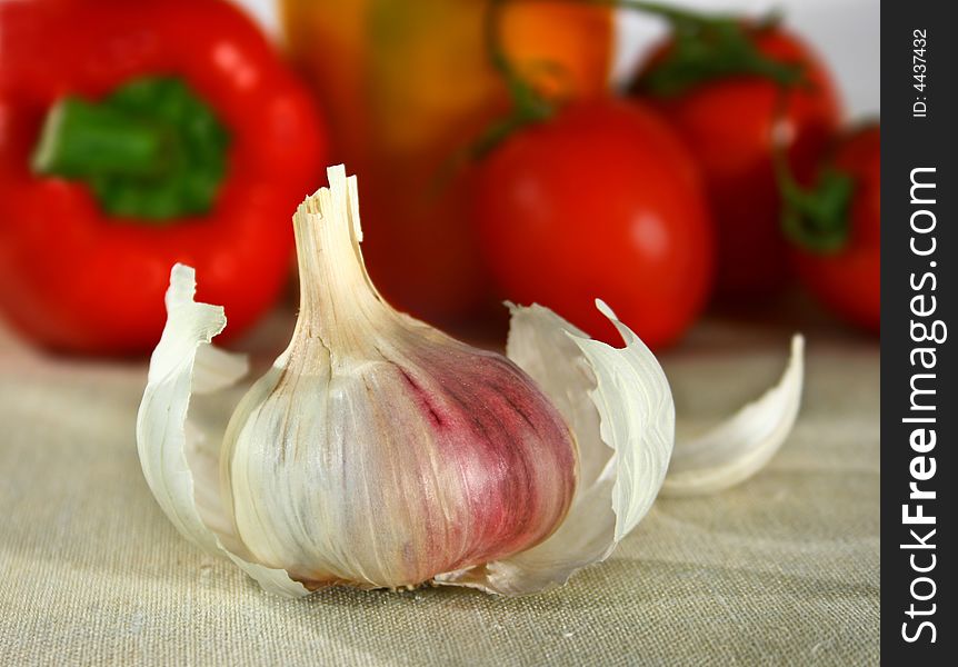Garlic  in front of pepper and tomato above flaxy tablecloth. Garlic  in front of pepper and tomato above flaxy tablecloth