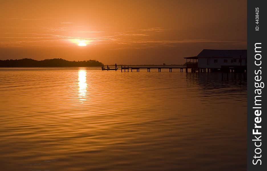 Sunrise in Oak Hill Florida with fishermen in silhouette approaching a dock at a fish camp. Bright orange sky