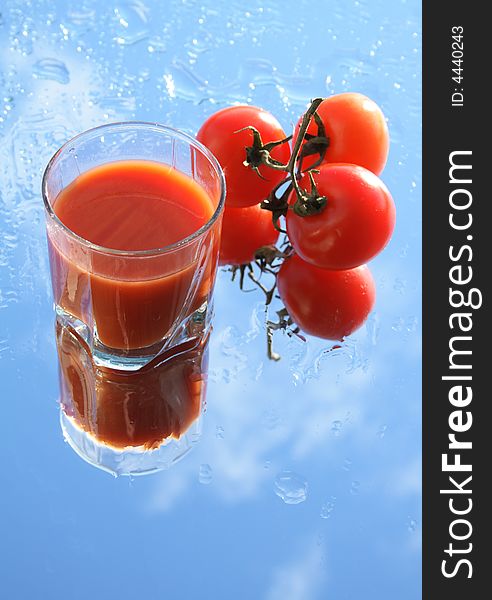 Glass of tomato juice on background with blue sky and three fresh tomatoes