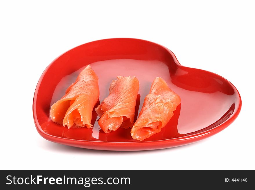 Three pieces of smoked salmon on red heart shape plate, white background, light shadow