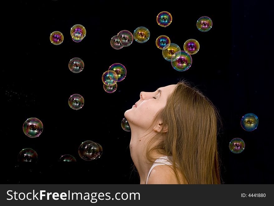 The teenage girl and soap-bubbles on the black background