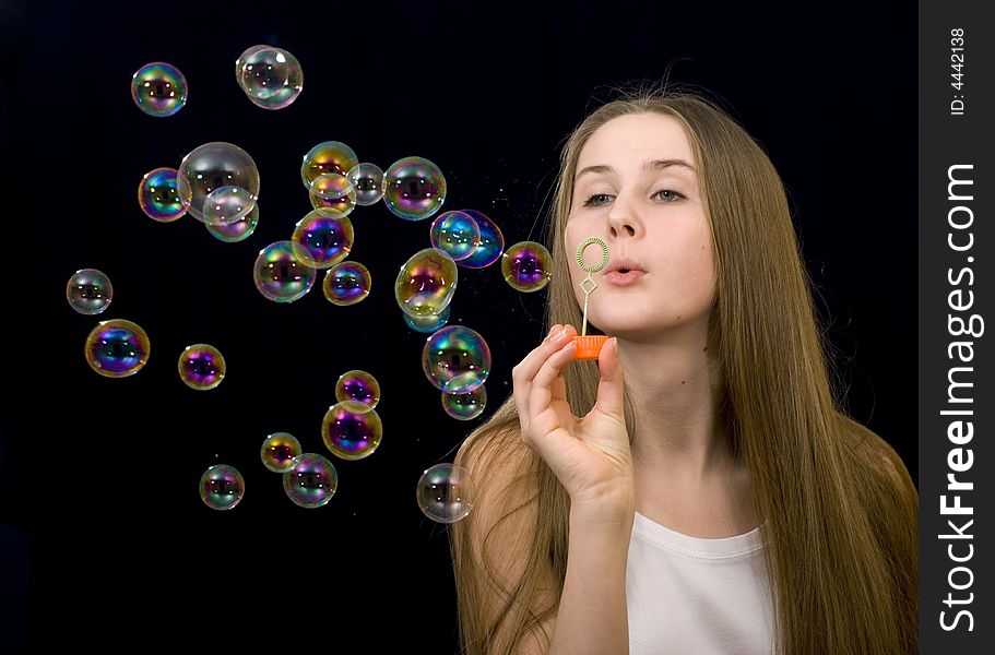 The teenage girl is blowing soap-bubbles on the black background