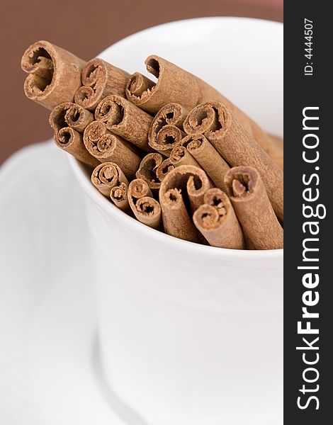 Close-up of a coffee cup filled with cinnamon sticks on brown background