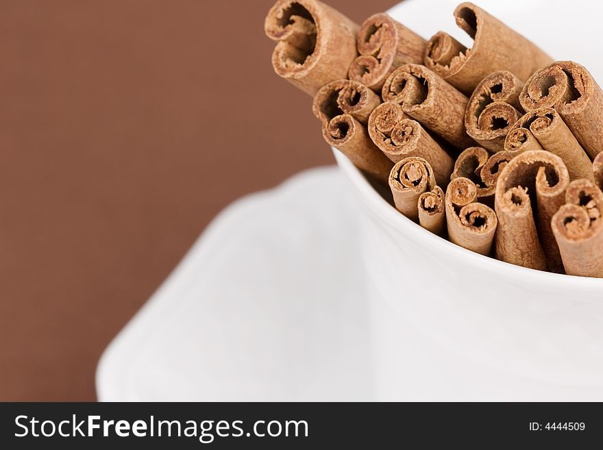 Close-up of a coffee cup filled with cinnamon sticks on brown background