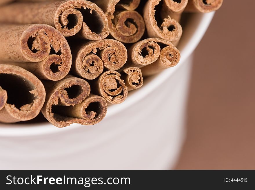 Close-up of a coffee cup filled with cinnamon sticks on brown background