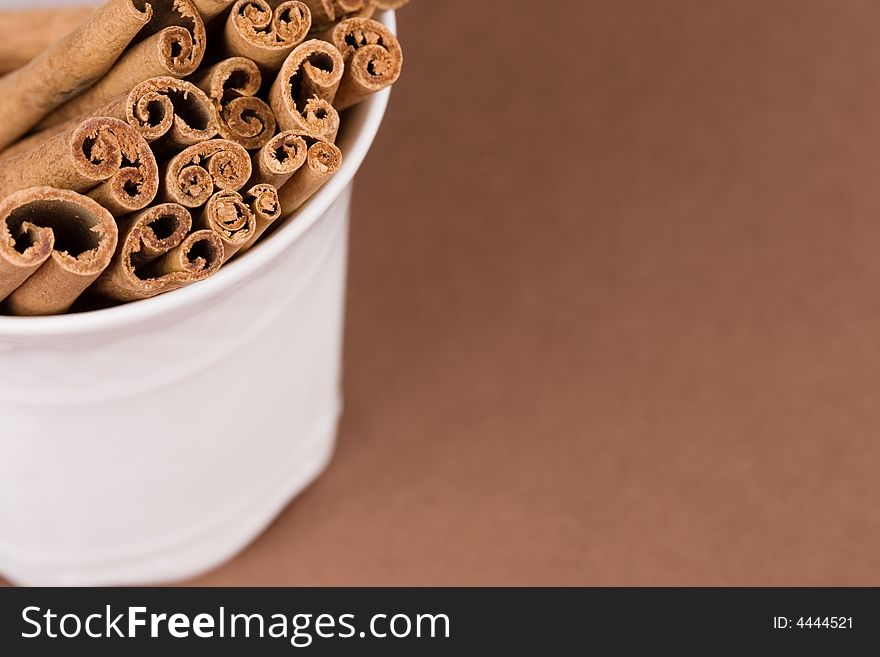 Close-up of a coffee cup filled with cinnamon sticks on brown background