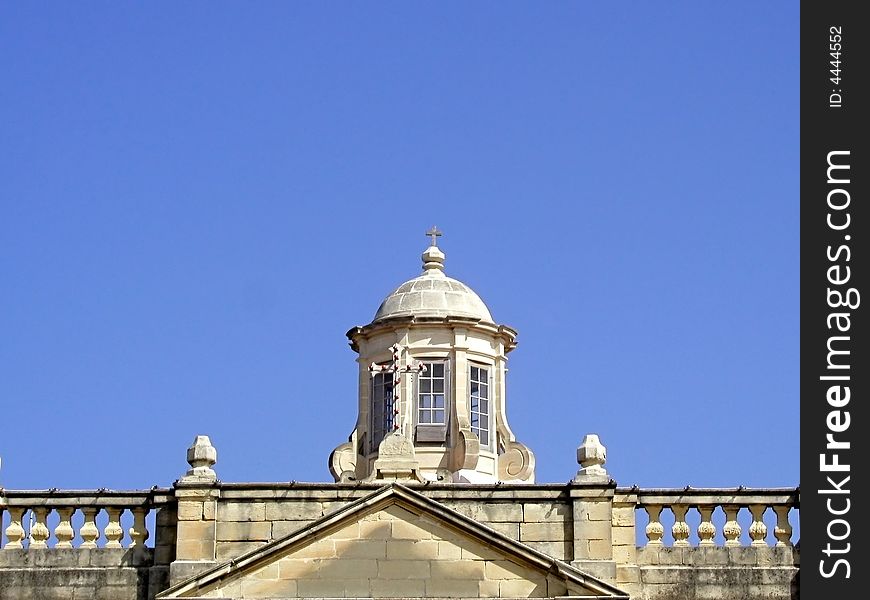 A traditional Maltese church top against clear blue sky.