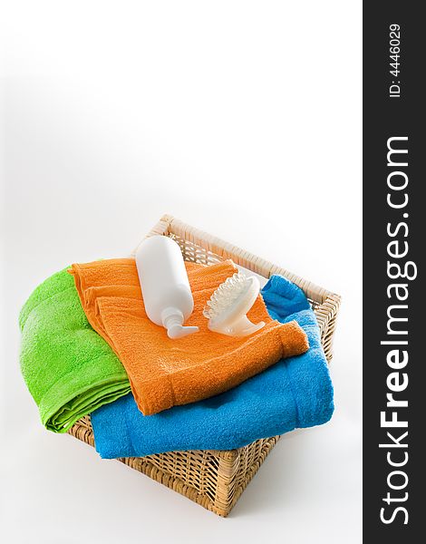 Mixed color bath towels, massager and lotion bottle in a square basket isolated on white background. Mixed color bath towels, massager and lotion bottle in a square basket isolated on white background.