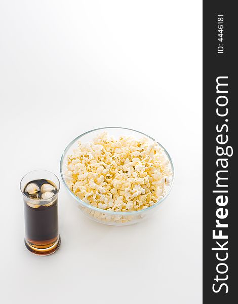 A glass bowl full with popcorn and a glass of cola with ice cubes isolated on white background. A glass bowl full with popcorn and a glass of cola with ice cubes isolated on white background.