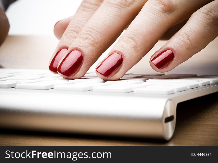 Fingers with red nail typing on keyboard