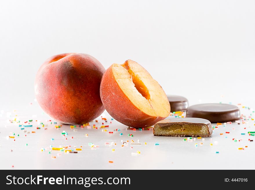 Whole and half peach, cream filled chocolate and sugar confetti on white background. Whole and half peach, cream filled chocolate and sugar confetti on white background.