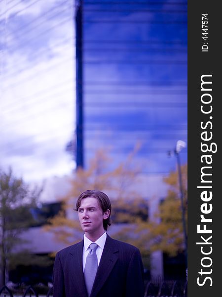Front view of single white businessman wearing suit standing in front of office building looking away. Front view of single white businessman wearing suit standing in front of office building looking away