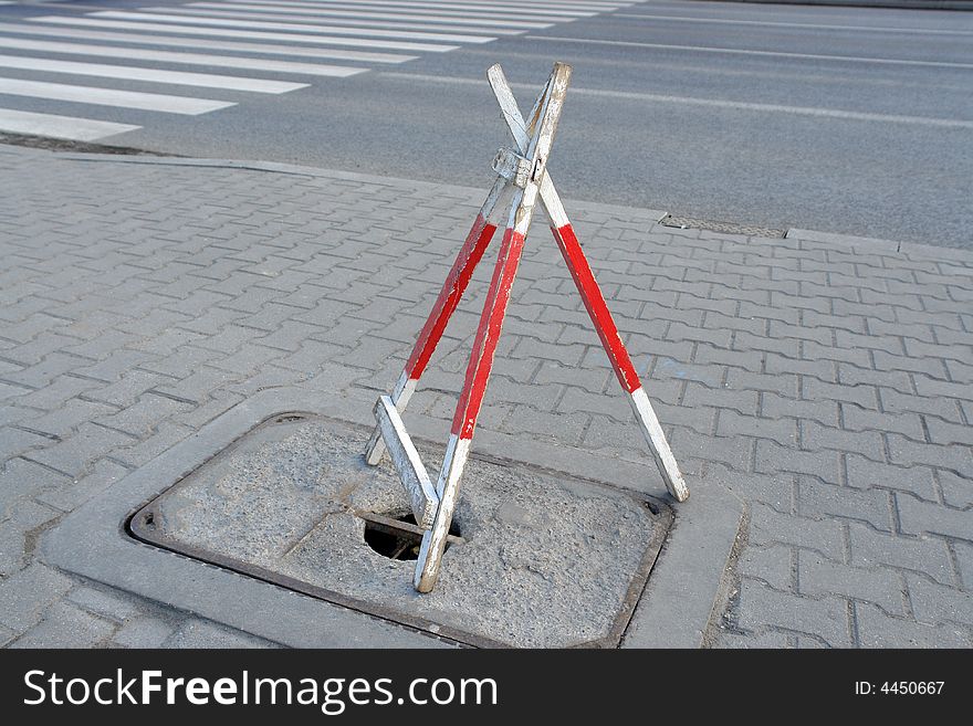 Wooden road tripod barrier placed over hole in sidewalk to protect pedestrians from falling into it