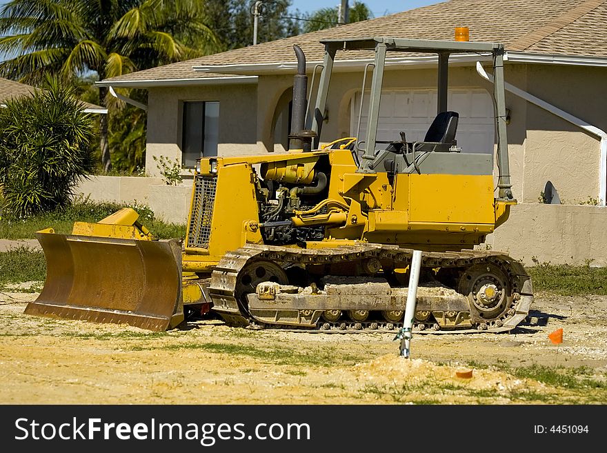A small bulldozer at rest at a job site with the blade rusting. A small bulldozer at rest at a job site with the blade rusting