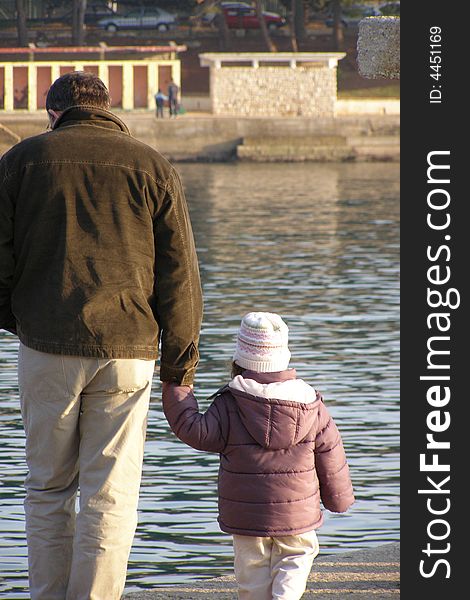Father and toddler daughter walking by the sea in winter, family quality time concept. Father and toddler daughter walking by the sea in winter, family quality time concept