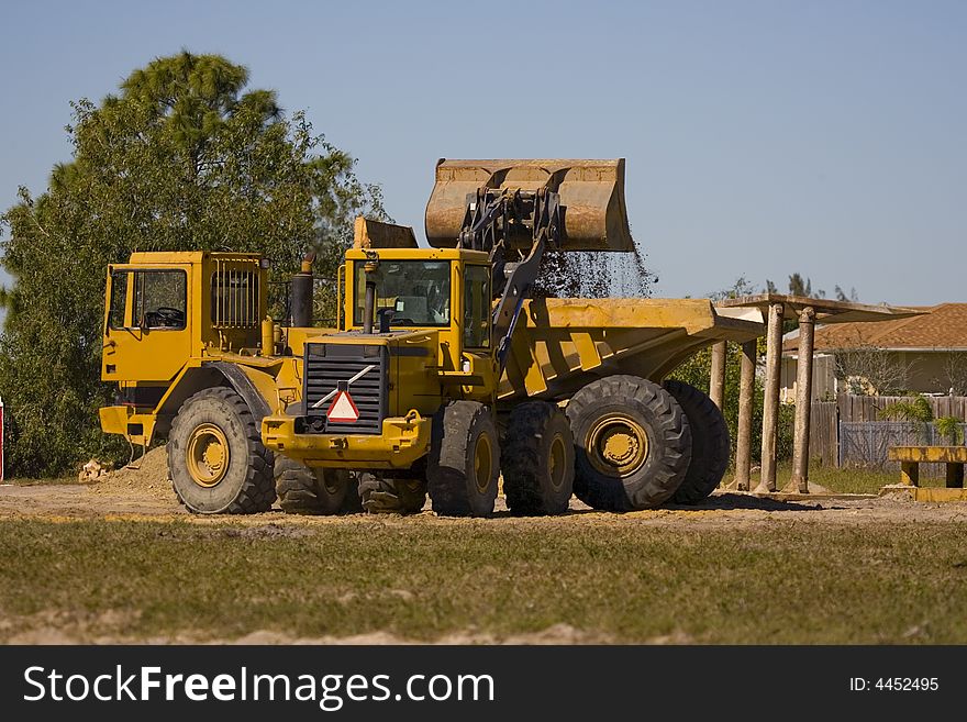 A front end loader is filling up the bed on a dump truck. A front end loader is filling up the bed on a dump truck